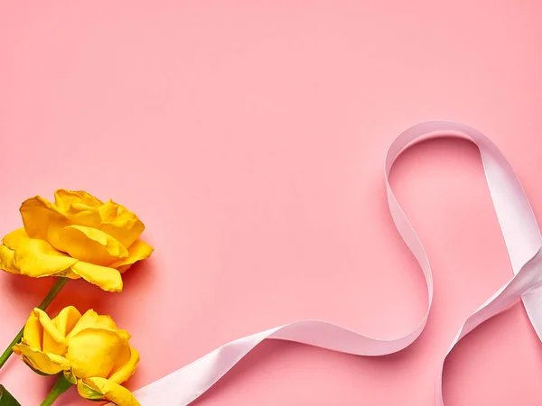 Pembe arka planda beyaz kurdeleli iki sarı gül.