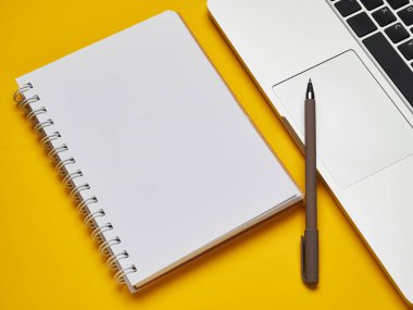 İş yeri - dizüstü bilgisayar, defter ve uzaktan kumandalı kalem sarı arka plan masası üzerinde. Ev ya da ofis için serbest bilgisayar. Kopyalama alanı olan arkaplan.