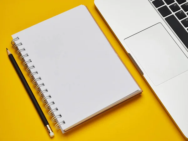 İş yeri - dizüstü bilgisayar, defter ve kalem sarı bir arkaplan masasında uzaktan çalışma için. Ev ya da ofis için serbest bilgisayar. Kopyalama alanı olan arkaplan.