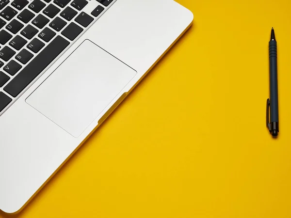 Sarı arka planda dizüstü bilgisayar ve kalem açın. Üst Manzara. mesaj için yer. çevrimiçi eğitim kavramı veya evde uzaktan çalışma.