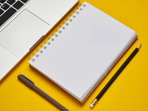 Workplace - laptop, notebook, pen, and pencil for remote work on a yellow background table. Freelance desktop for home or office. Background with copy space.