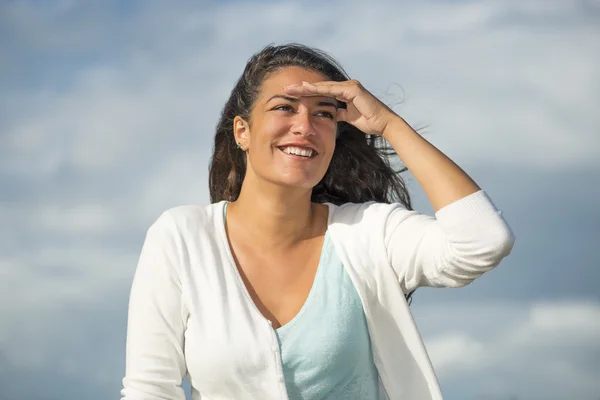Молодая женщина улыбается и экранирует глаза на фоне неба Лицензионные Стоковые Фото