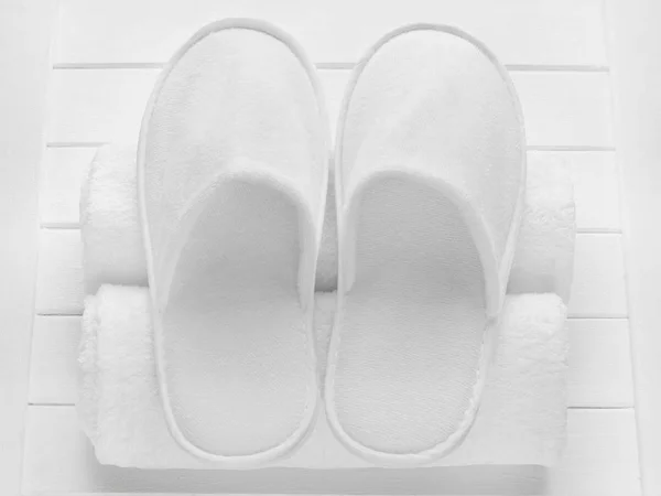 Pair of white hotel, home, spa,  wellness slippers with rolled towels on light wooden desk