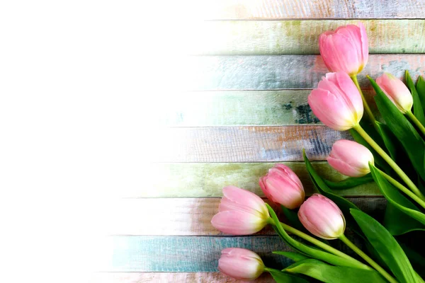 Bouquet of pink fresh tulips on colored wooden background with space for text - overhead view