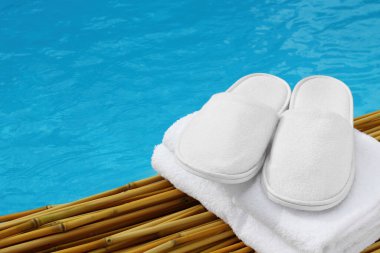 White hotel / home/ spa / wellness slippers with towel on bamboo wood with swimming pool - water - sea background with space for text - summer time