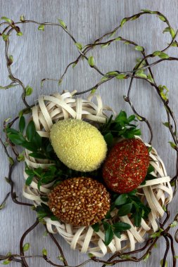 Paskalya süslemeleri / kartlar elle dekore edilmiş Paskalya yumurtaları alışılmadık bir şekilde baharat ve kuskus ile kaplı ahşaptan yapılmış bir yuvada söğüt çubuklarıyla masanın üzerinde