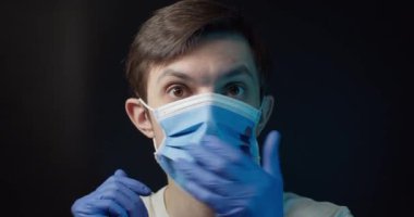 Bir adam tıbbi bir maske takıyor ve çıkarıyor.