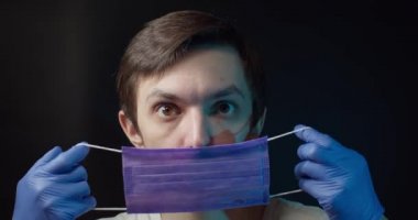Bir adam tıbbi bir maske takıyor ve çıkarıyor.