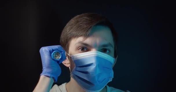 Un uomo in maschera medica guarda la macchina fotografica con una torcia elettrica — Video Stock