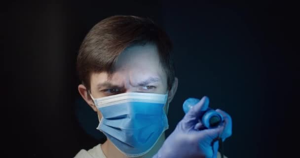 En man i en medicinsk mask tittar på sig själv med en ficklampa och nyser — Stockvideo