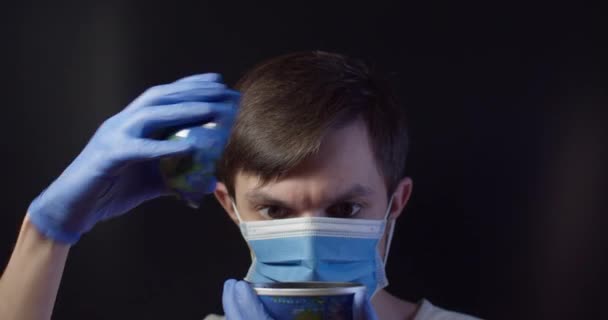Um homem com uma máscara médica põe um comprimido num globo — Vídeo de Stock