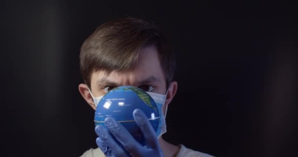 Человек в медицинской маске исцеляет глобус от болезни, сжимая шприц. — стоковое видео