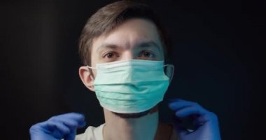Bir adam tıbbi bir maske takıyor ve çıkarıyor.