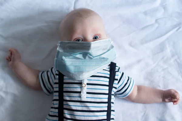 Bebek mavi halıya uzanmış, maske takmış.