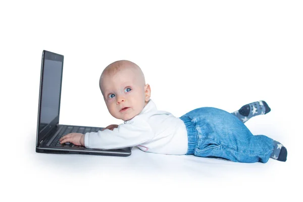 赤ちゃん男の子横たわっ彼の胃身に着けている白いシャツと青いジーンズ作業に黒のラップトップ右上を見てと思う — ストック写真