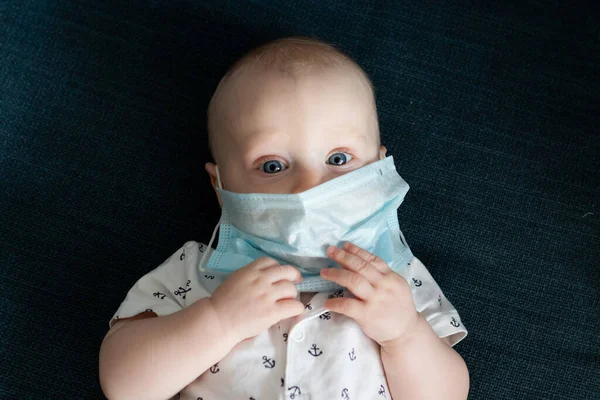 Beyaz, beyaz, beyaz, beyaz, beyaz, beyaz, beyaz bir erkek bebek. Bir dairede mavi bir maske takıyor. Coronavirus kovid sırasında 19 kez kendini izole edip yüzünü ve burnunu kapatan maskesine dokunuyor.