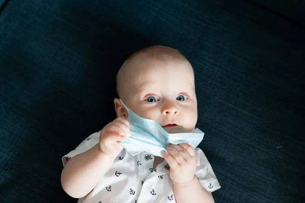 Beyaz, beyaz, beyaz, beyaz, beyaz, beyaz bir erkek bebek. Bir dairede mavi bir maske takıyor. Coronavirus kovid sırasında 19 kez kendini izole ediyor ve maskesine dokunuyor.