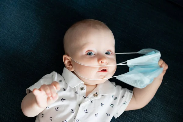 Beyaz, beyaz, beyaz, beyaz, beyaz, beyaz, beyaz, beyaz bir erkek bebek. Bir dairede mavi bir maske takıyor. Coronavirus kovid sırasında 19 kez kendini soyutlama ve karantina yüzünden evde kalıyor.