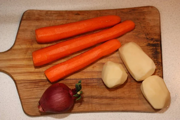 Red onion, peeled potatoes and carrots on the dirty chopping board. Top view. — Stock Photo, Image