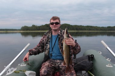 A fisherman in polarized glasses caught a pike clipart