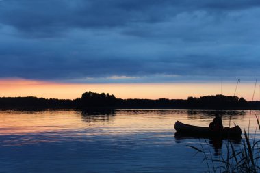 Günbatımı Vuoksa Gölü ve bir tekne bir balıkçı silüeti.