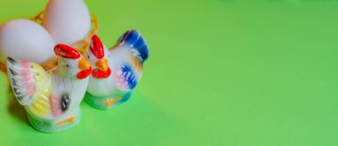 Yeşil arka planda bir sepetin içinde bir horoz, tavuk ve yumurta figürü olan güzel bir Paskalya süslemesi. Boşluğu kopyala