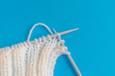 Yün ipliğinden bir eşarp örüyorum. Adım adım. Örgü örmeyi öğreniyorum. Mavi arka planda beyaz ipliklerden yapılmış eşarp. evde eğitim