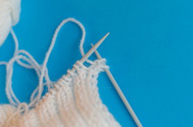 Yün ipliğinden bir eşarp örüyorum. Adım adım. Örgü örmeyi öğreniyorum. Mavi arka planda beyaz ipliklerden yapılmış eşarp. evde eğitim