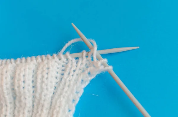 Knitting a scarf from wool yarn. Step by step. Learning to knit. Scarf made of white threads on a blue background. home schooling