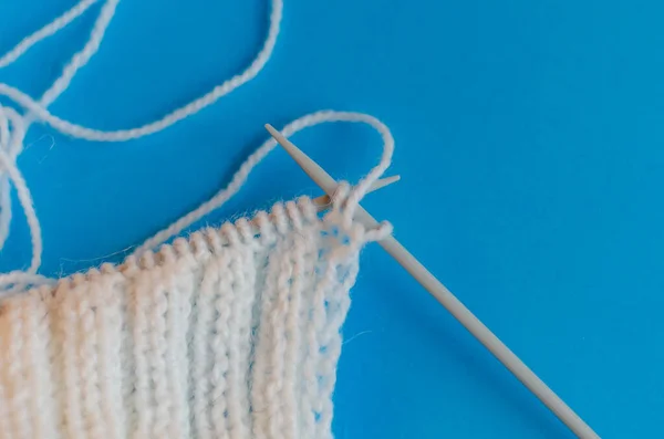 Knitting a scarf from wool yarn. Step by step. Learning to knit. Scarf made of white threads on a blue background. home schooling