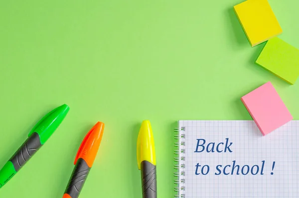 Texte "Retour à l'école" sur le carnet. Fournitures scolaires et de bureau sur table de bureau, fond vert. Pose plate, espace de copie . — Photo
