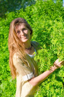 Parktaki genç sarışın kadın, güneşli bir günde bir dala uzanır..