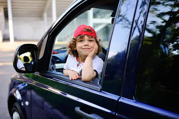 Kıvırcık saçlı, kırmızı bere çocuk arabanın direksiyonuna oturur — Stok fotoğraf