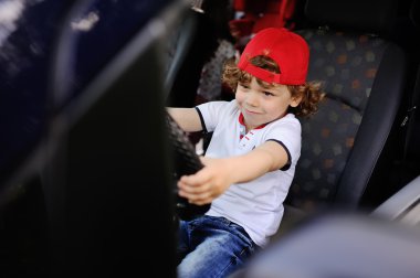 kıvırcık saçlı, kırmızı bere çocuk arabanın direksiyonuna oturur