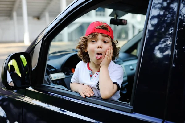 Child with curly hair and a red cap sits behind the wheel of  car — Stock Photo, Image