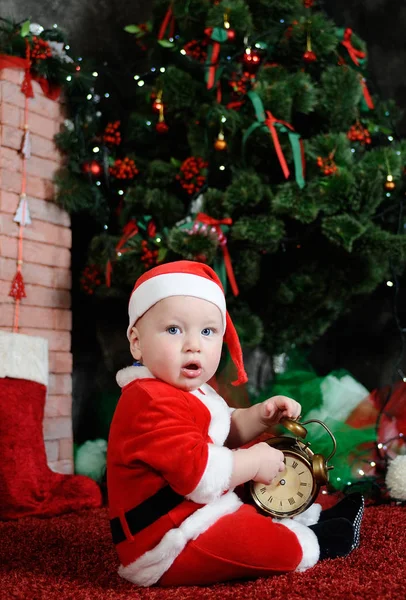 Child dressed as Santa Claus holding a clock alarm.  dresse — Stock Photo, Image