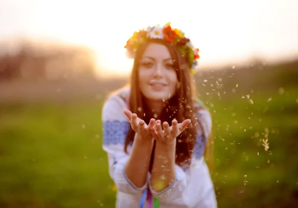 Fille dans une couronne de fleurs sur sa tête souffle la peluche de salut — Photo