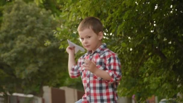 Kleine jongen lanceert een papier vliegtuig. — Stockvideo