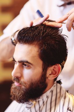 Kuaför bir sakal ve bıyık yakışıklı bir genç adam için bir saç kesimi yapıyor