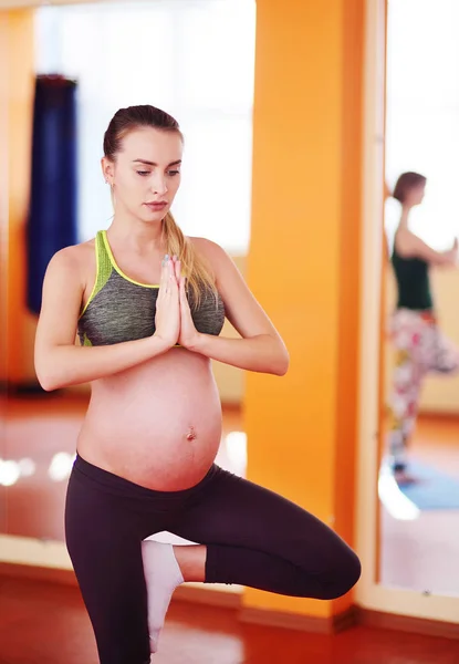pregnant woman performs aerobic exercises or asanas with a group of yoga in a fitness room.