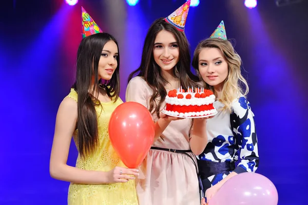 Tre flickor i festliga hattar och ballonger och tårta i handen. — Stockfoto