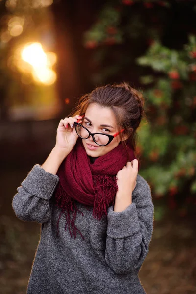 Dívka v brýlích a s červeným šátkem jho na krku proti zapadajícímu slunci — Stock fotografie