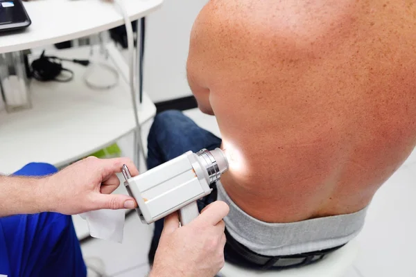 The dermatologist examines the moles or acne of the patient with a dermatoscope.
