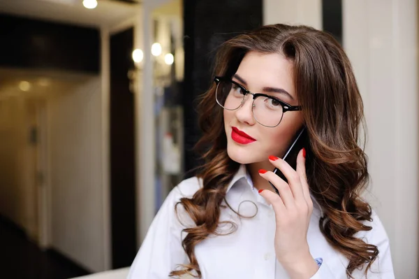 Beautiful young girl in a white shirt and glasses talking on a mobile phone — Stock Photo, Image