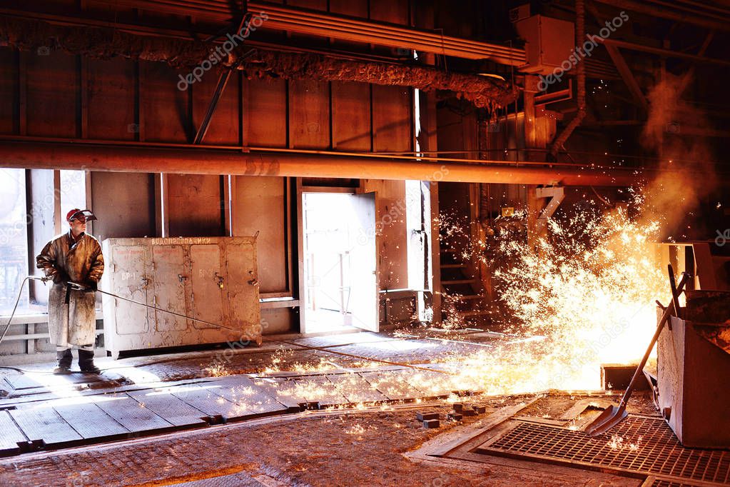 Liquid metal is poured into molds. Worker, controlling the melting of metal in furnaces. A man works at a metallurgical plant against a blast furnace