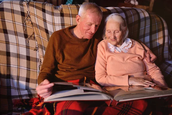 Пожилая пара рассматривает семейный фотоальбом, завернутый в клетку — стоковое фото