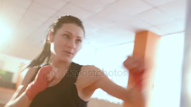 Chica en ropa deportiva y vendajes de boxeo rojo supera a una pera de boxeo en el gimnasio — Vídeos de Stock