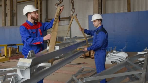 Werknemers in de fabriek laden de lading op de haak van de kraan tegen de achtergrond van de productie — Stockvideo