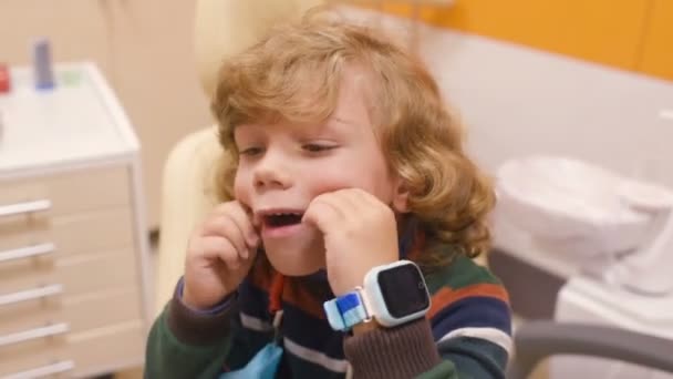 Enfant aux cheveux bouclés se livre et grimace dans une chaise dentaire — Video
