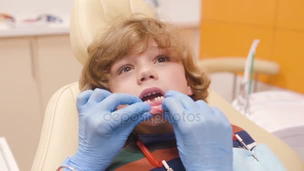 Kudrnaté vlasy dítě oddává a grimasy v zubařském křesle — Stock video